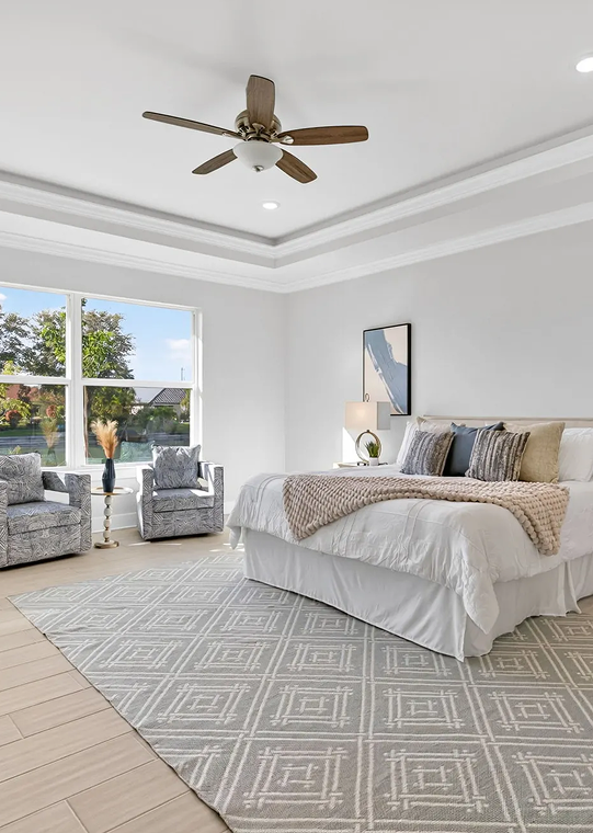 Bright bedroom with bed, ceiling fan, chairs by window