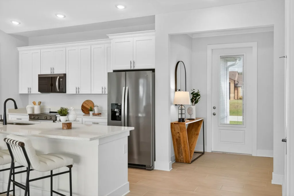 White kitchen with island, stainless refrigerator, and entry door.