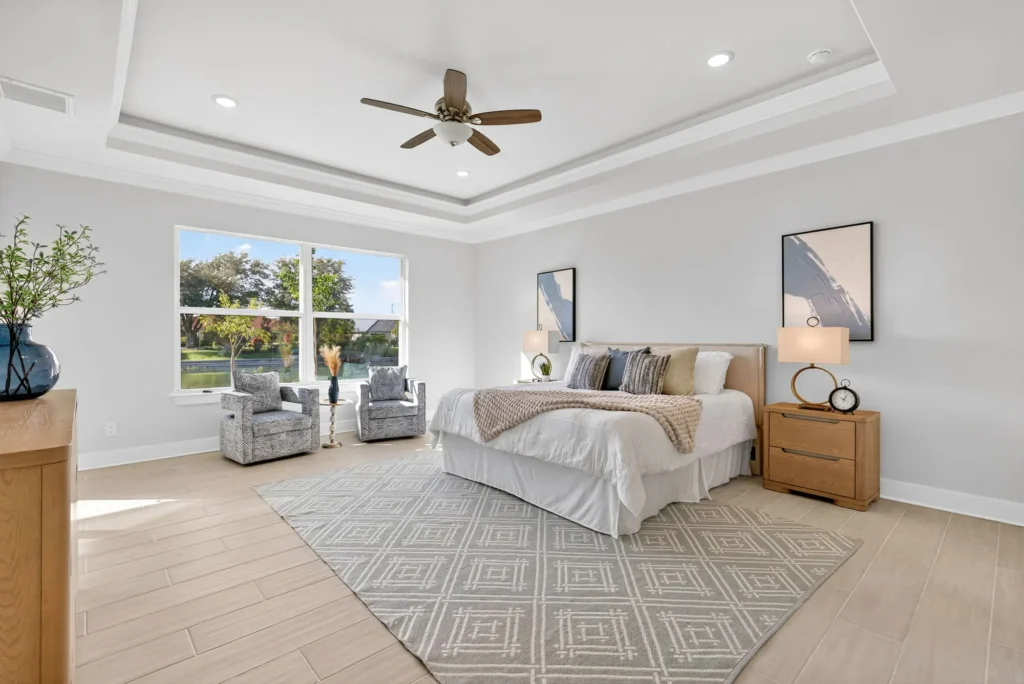 Bright bedroom with large window, bed, chairs, ceiling fan.