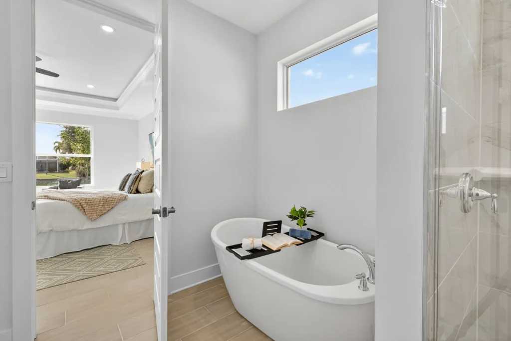Freestanding bathtub with tray beside glass shower and bedroom view