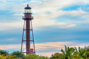 Tall lighthouse tower above palm trees under cloudy sky