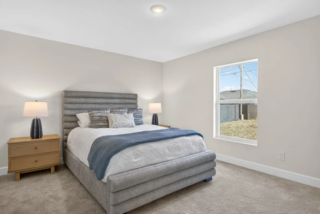 Bedroom with gray upholstered bed, nightstands, lamps, and window