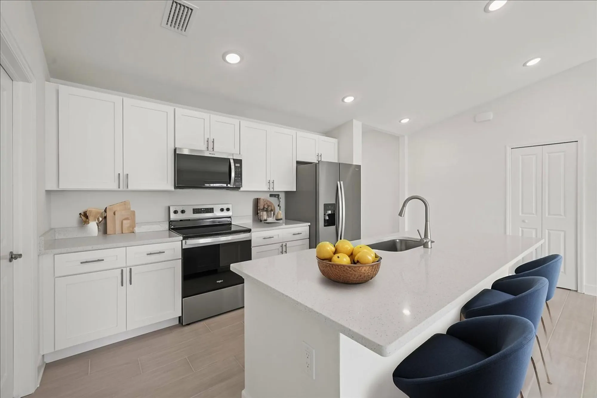 White kitchen with island, stainless appliances, blue bar stools