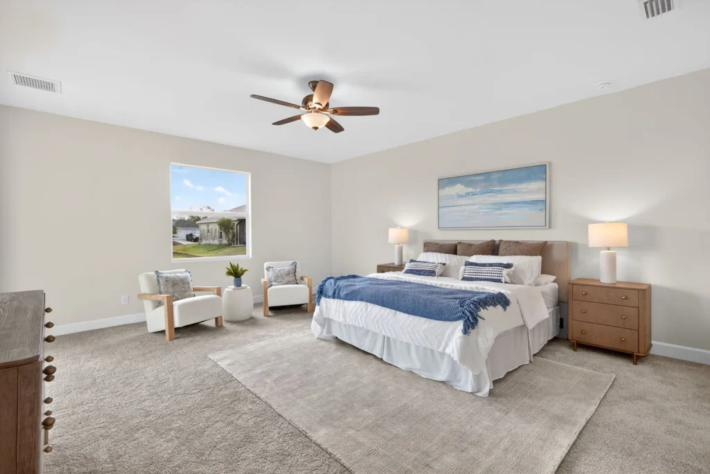 Staged bedroom with king bed, chairs, ceiling fan.