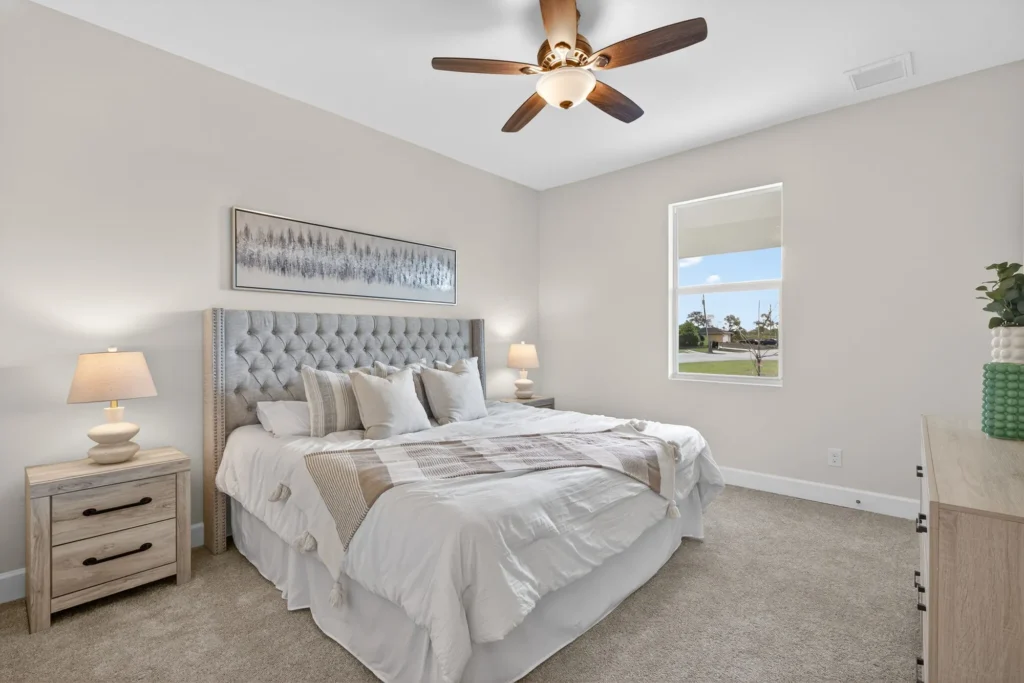 Staged bedroom with tufted bed, ceiling fan, and window