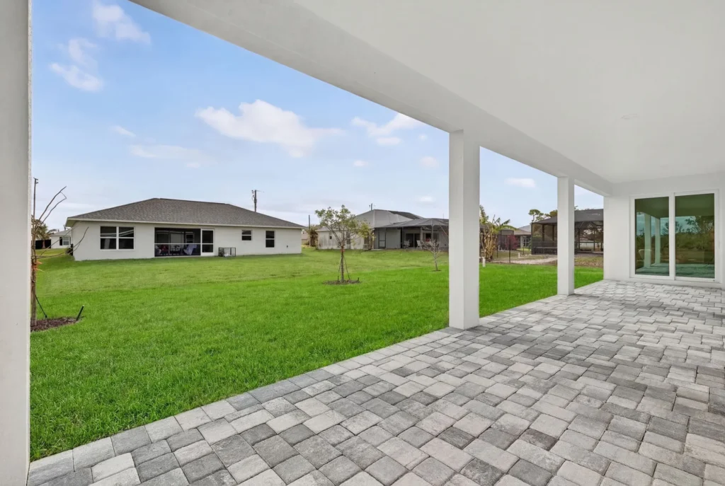 Covered patio with pavers overlooking grassy backyard and houses