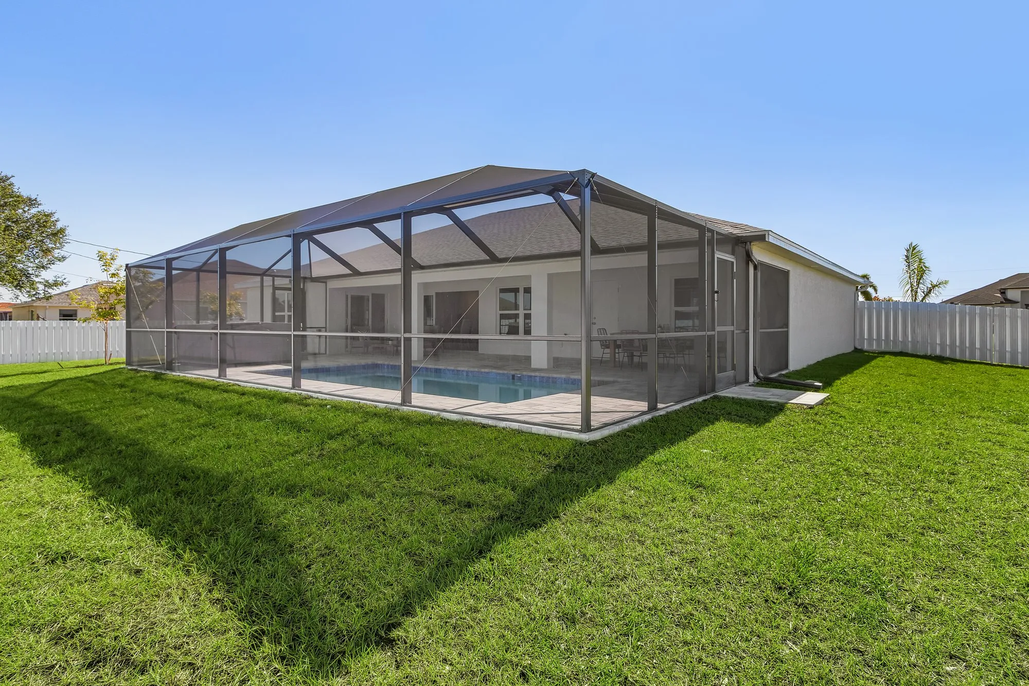 Backyard screened pool enclosure beside single-story home