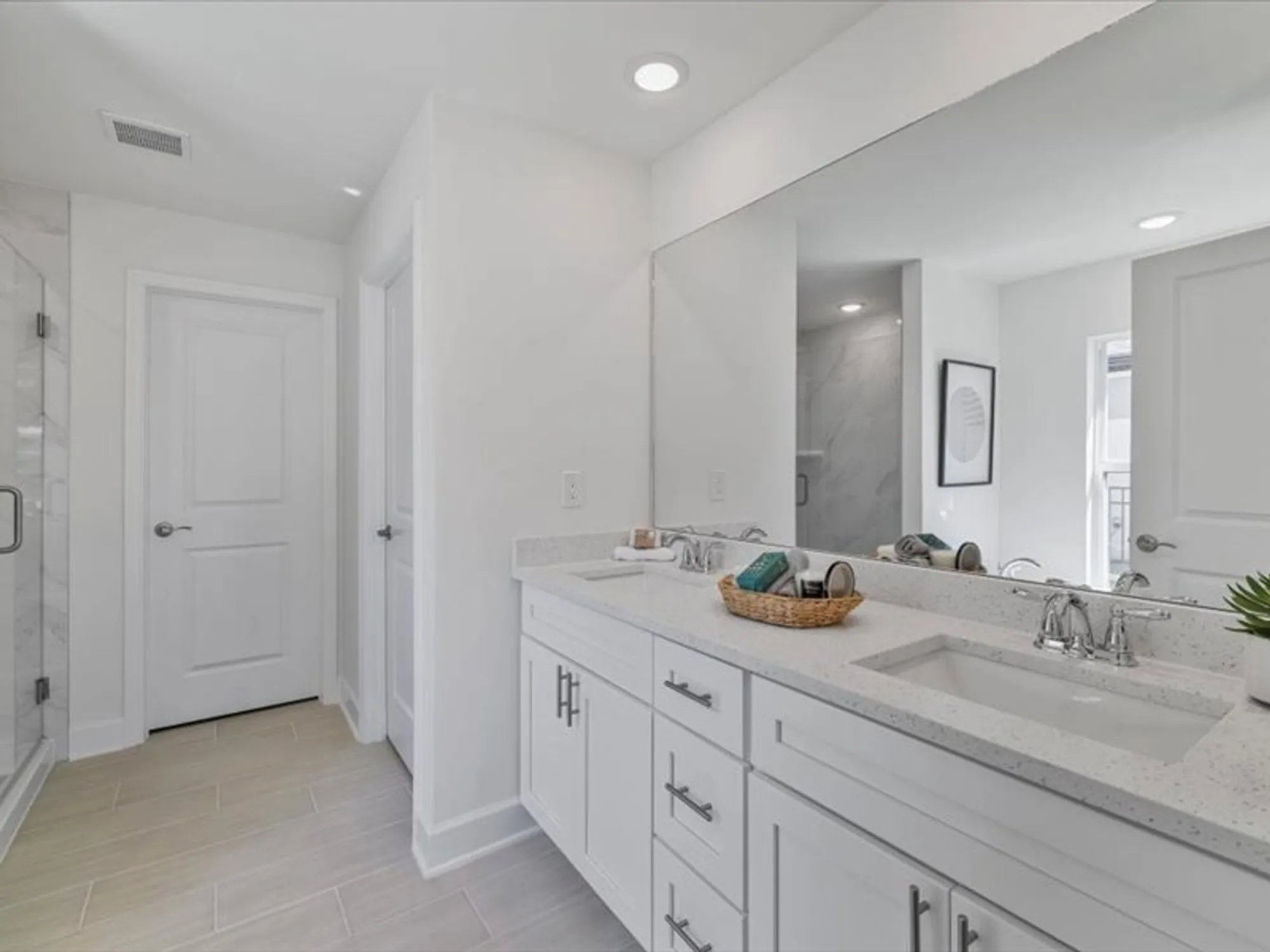 Bright bathroom with double vanity, large mirror, and shower