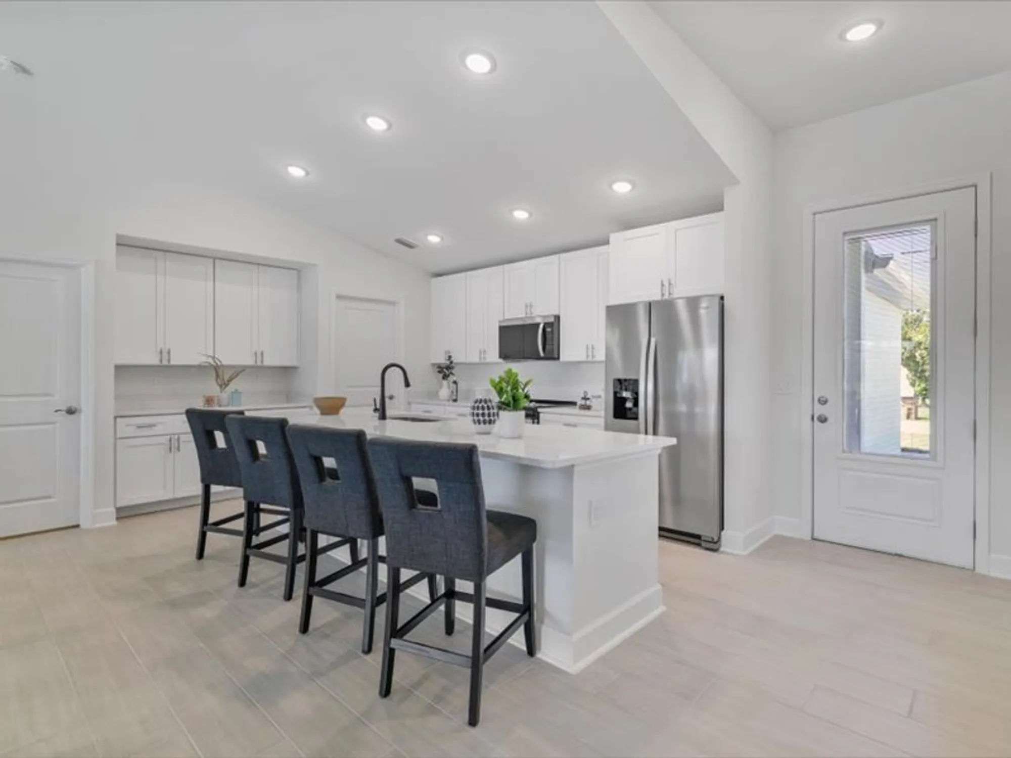 Bright white kitchen with island, three stools, stainless appliances