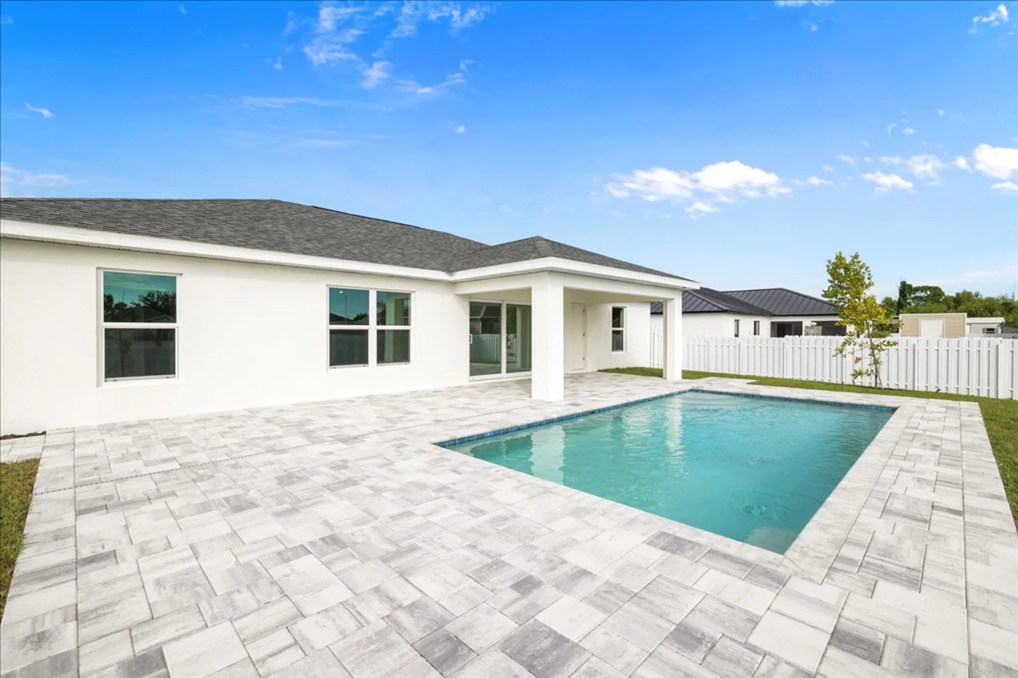 Backyard pool and paver patio behind modern white house