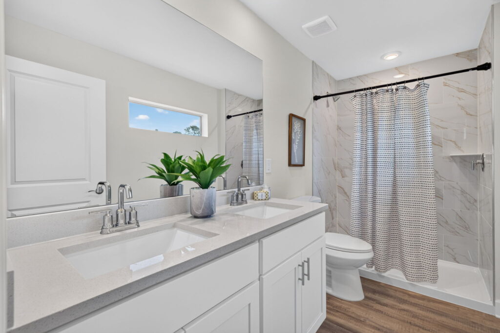 Bright bathroom with double vanity, toilet, shower curtain