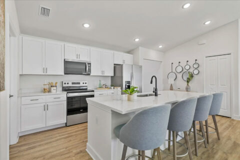 Model home kitchen with white shaker cabinets, a quartz island and blue counter stools